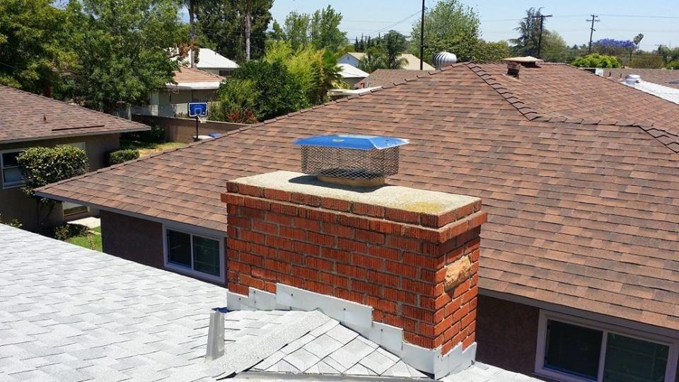 Refaced brick chimney on a tile roof under a clear sky
