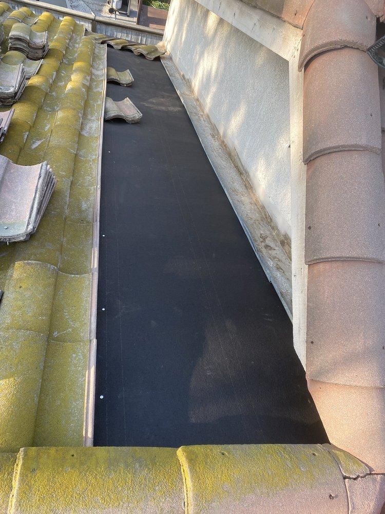 Freshly installed step flashing around a chimney on a tile roof